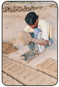 Image D- a man is putting mud into the stencil to get the shape of a brick.