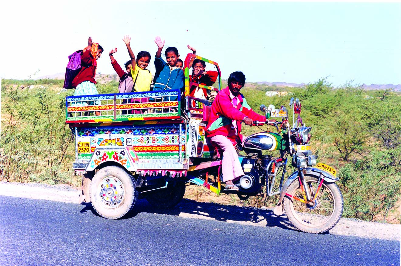 कुछ बच्चे मोटर-बाइक पे बैठे हैं जो पीछे से लकड़ी के फट्टों से बनी है  