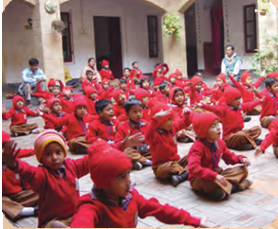 स्कूल के फर्श पर कुछ बच्चे बैठे हैं