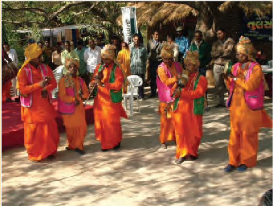 एक खुले क्षेत्र में, एक पार्टी में कुछ लोग इकट्ठा  हैं और कुछ पुरुष धोती कुर्ता पहने और सिर पर पगड़ी पहने उनके मुंह से वाद्य बजा रहे हैं।