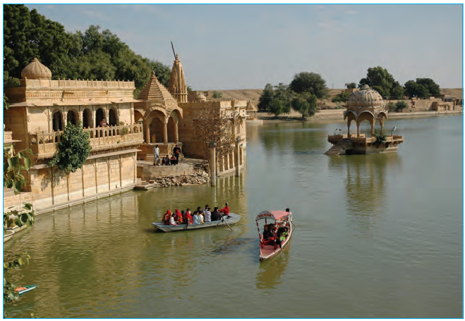 घड़सीसर का चित्र जिसमें कुछ लोग झील में नौका विहार कर रहे हैं और झील के पास पुराना किला है। 