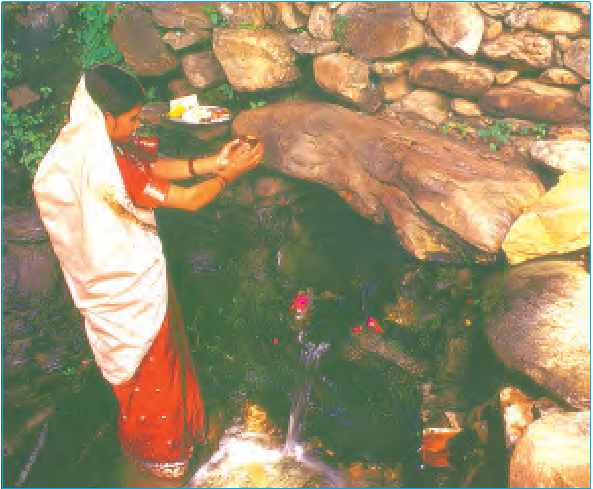 एक महिला दुल्हन के रूप में तैयार हुई और चट्टानों के पास एक छोटे से तालाब की पूजा कर रही है।  