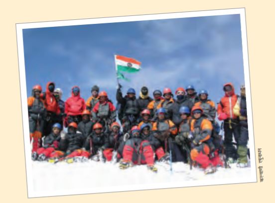 लोगों का एक समूह, जिसमें कुछ बैठे हैं और कुछ खड़े हैं, उनमें से एक भारत का झंडा पकड़े हुए है।