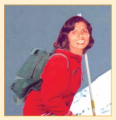 कंधे पर बैग और हाथ में डंडा लिए एक लड़की बर्फीले पहाड़ पर चढ़ रही है।