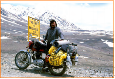 एक आदमी अपनी मोटरसाइकिल के साथ पहाड़ों के पास सड़क पर।