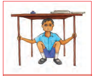 एक मेज के नीचे बैठा एक लड़का मजबूती से उसकी बाँहों को पकड़े हुए है।