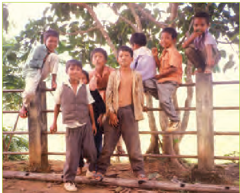 एक रैलिंग के सहारे खड़े कुछ बच्चे।  पीछे पड़ी नदी और कुछ पेड़ हैं।