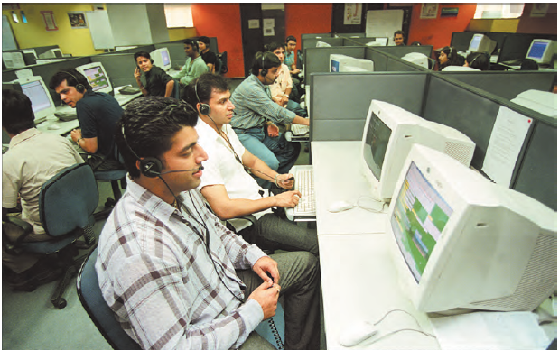 एक कार्यस्थल जिसमें बहुत से लोग कंप्यूटर स्क्रीन के सामने बैठे हैं और हेडफ़ोन पहने हुए हैं।  