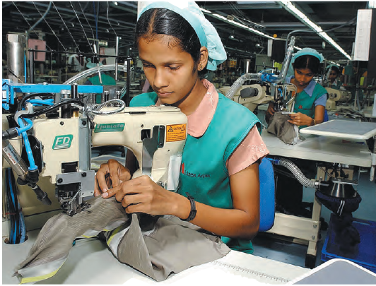 कपड़े निर्यात वाली एक कंपनी के कार्यालय में लड़कियां सिलाई मशीन पर कपड़े सिल रही हैं। 