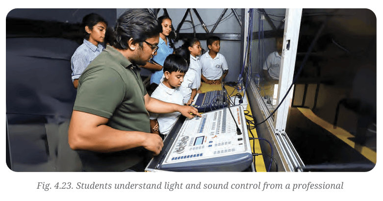 Students gathering around an auditorium control console while a professional explains light and sound control systems.