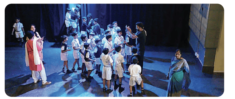A group of students on stage during a rehearsal session with their teacher/director